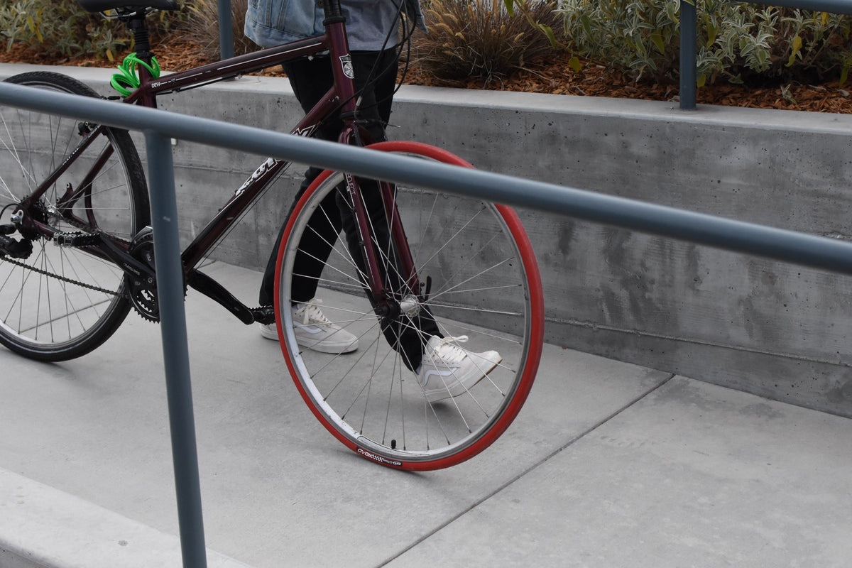 a student walks his bike down a ramp, the bike has a red front tire, the bike belongs to rental / subscription company MiBike